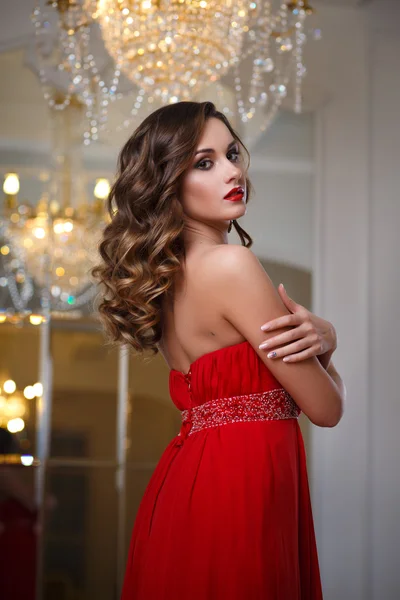 Hermosa mujer joven con maquillaje perfecto y estilo de pelo en magnífico vestido de noche rojo en el interior de lujo caro — Foto de Stock