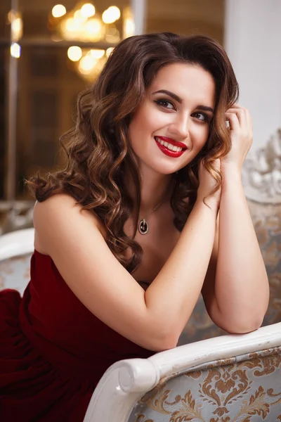 Beautiful young woman with perfect make up and hair style in gorgeous red evening dress in expensive luxury interior Royalty Free Stock Photos