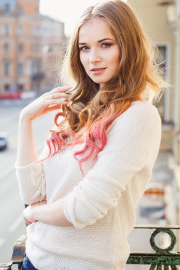 Portrait of young lady wearing white pullover posing on a balcony