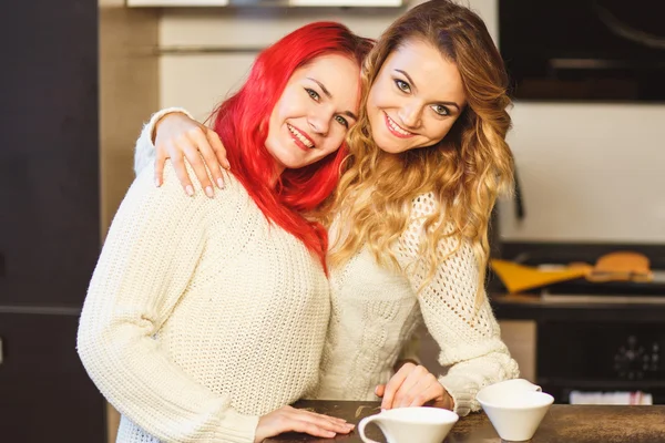 Portret van twee lachende meisjes vrienden in witte truien over keuken achtergrond — Stockfoto