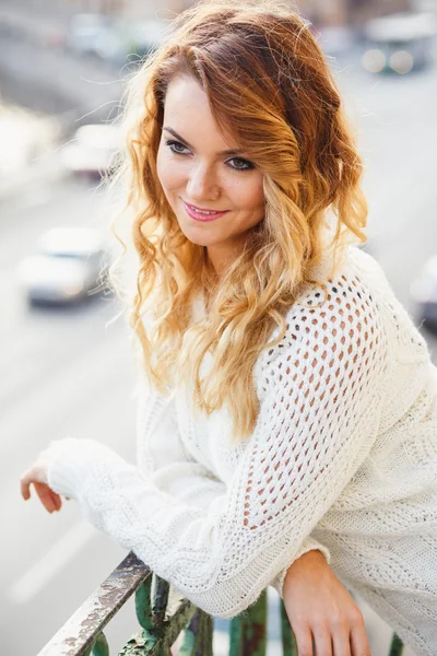 Portrait of young lady wearing white pullover posing on a balcony — Stockfoto