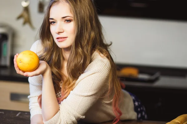 Porträtt av unga blonda kvinnan i ett kök håller orange — Stockfoto