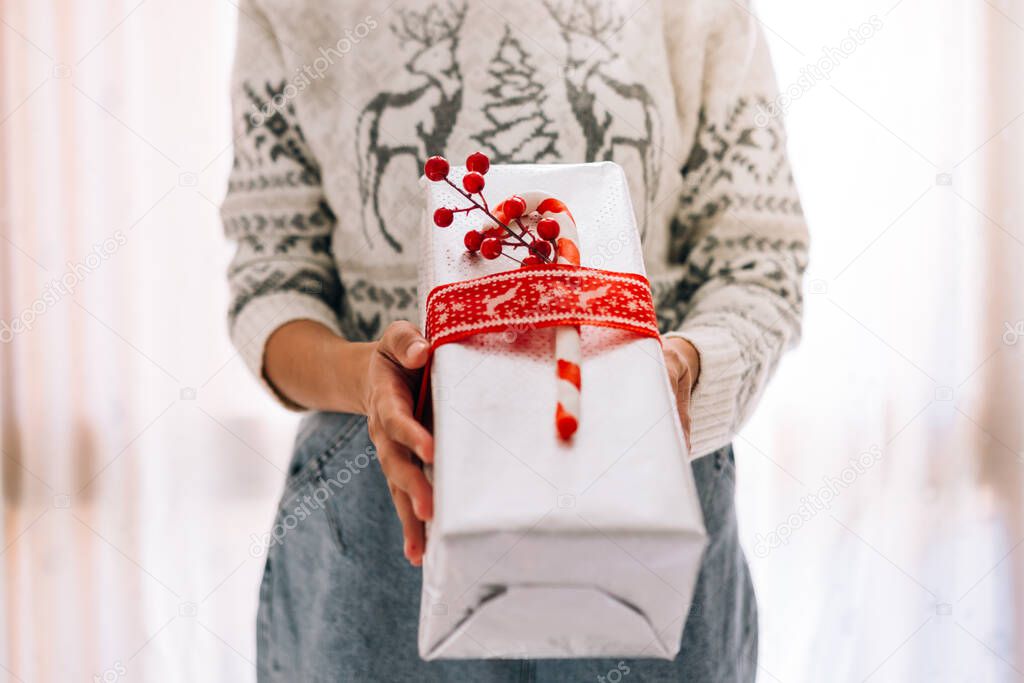 Young unrecognizable woman holds in a gift box in metallic paper with red twine and candy. Christmas New Years present.