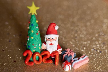 Oyuncak killi noel konsepti. Renkli el yapımı minyatür Noel ağacı, hediyeler ve altın arka planda Noel Baba. 2021 Yeni Yıl.