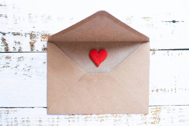 Beyaz ahşap zemin üzerinde kil kırmızı kalp olan bir zarf içinde aşk mektubu..