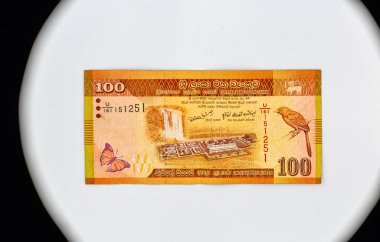 100 Sri Lanka Rupisi, fotokopi alanına yakın çekimde kullanılmış. Norochcholai Kömür Santrali Projesi ve Laxapana Şelalesi, Sri Lanka turuncu gagalı geveze, faturada güz yaprağı kelebeği.