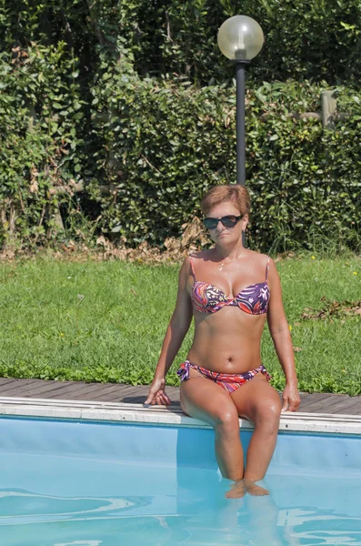 Mulher caucasiana sentado na borda da piscina exterior — Fotografia de Stock