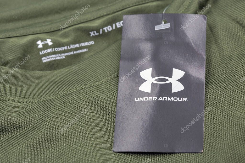 Kyiv, Ukraine - June 23, 2025: Olive green Under Armour loose fit athletic shirt with black branded hang tag and iconic logo, size XL marking and product specifications on performance sportswear.