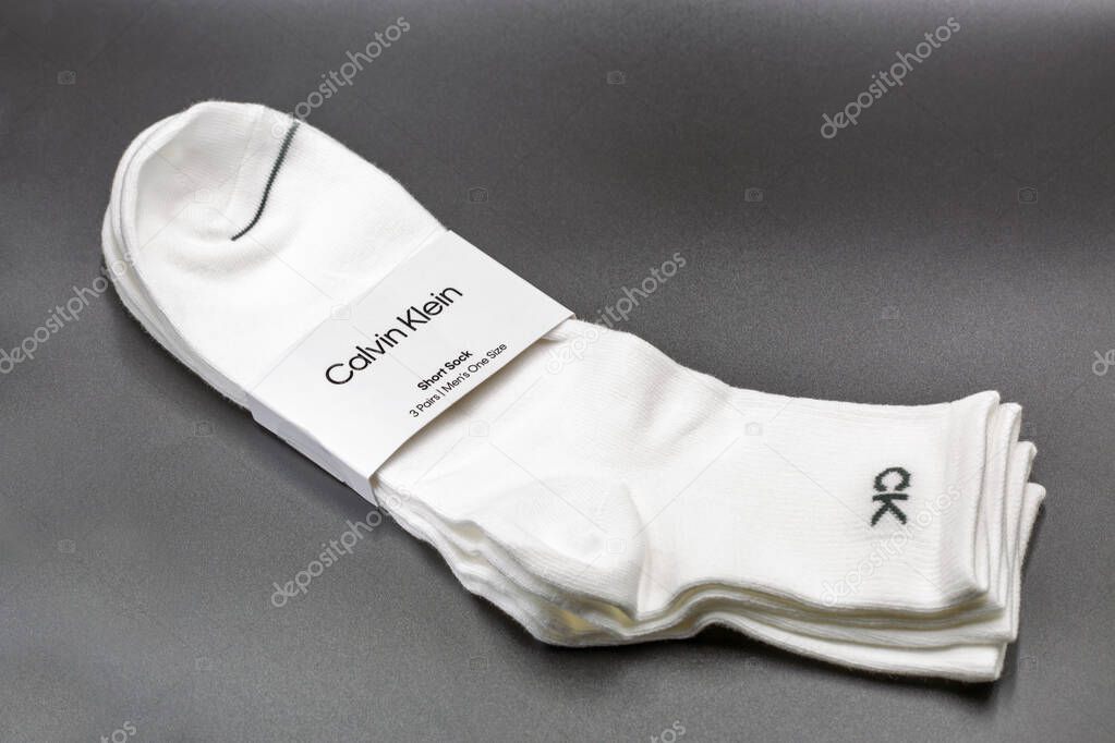 Kyiv, Ukraine - July 19, 2025: Three pair pack of Calvin Klein branded white short ankle socks with CK logo detail and paper wrapper band, men's casual hosiery accessories on black background closeup.