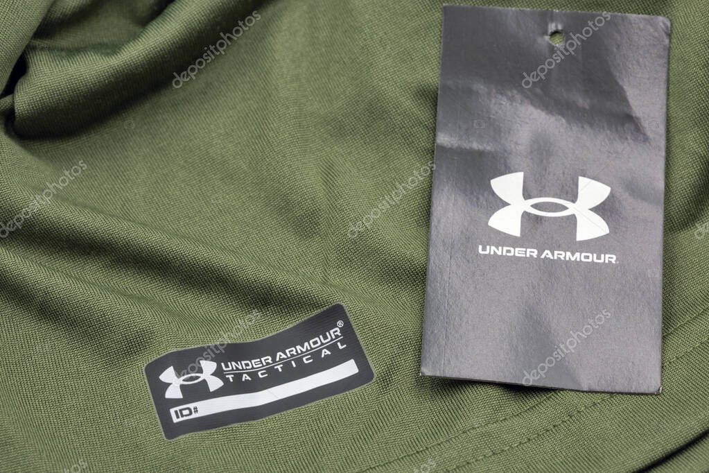 Kyiv, Ukraine - June 23, 2025: Olive green Under Armour loose fit athletic shirt with black branded hang tag and iconic logo, marking and product specifications on performance sportswear.