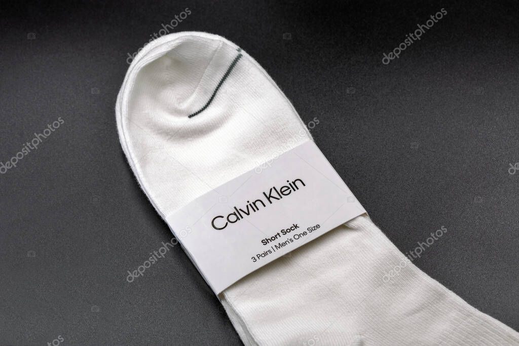 Kyiv, Ukraine - July 19, 2025: Three pair pack of Calvin Klein branded white short ankle socks with CK logo detail and paper wrapper band, men's casual hosiery accessories on black background closeup.