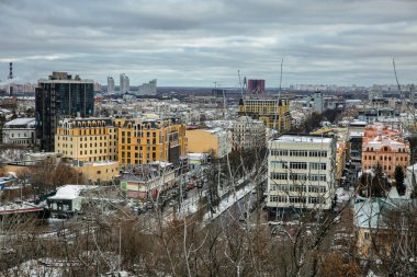 Kyiv 'in kışın tarihi Podil bölgesinin hava manzarasında, karla kaplı çatıları ve bulutlu gökyüzü altındaki sarı apartman blokları da dahil olmak üzere renkli konut ve ticari binaların karışımı yer alıyor..