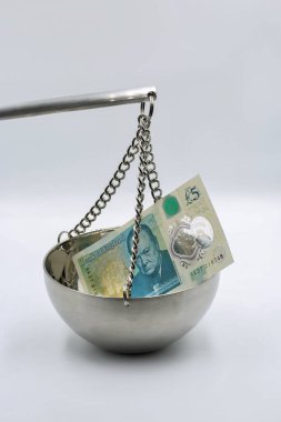 Beş sterlinlik banknot, Winston Churchill 'in portresinin metalik asma kabına konması, finansal dengeyi, mali ağırlığı ve İngiliz maliyesindeki ekonomik adaleti sembolize ediyor..