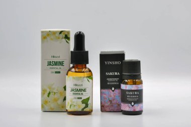 Kyiv, Ukrayna - 14 Aralık 2024: Hllozzi Jasmine ve Yinsho Sakura ambalaj kutularıyla gerekli yağ şişeleri, aromaterapi için kehribar cam damlaları, beyaz üzerine doğal sağlık ürünleri.