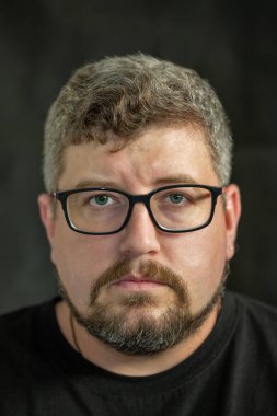 Siyah arka planda gözlüklü, kızıl saçlı, sakallı ve bıyıklı beyaz bir adamın stüdyo portresi..