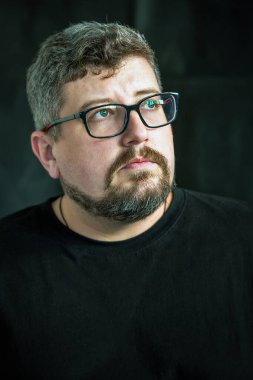 Siyah arka planda gözlüklü, kızıl saçlı, sakallı ve bıyıklı beyaz bir adamın stüdyo portresi..