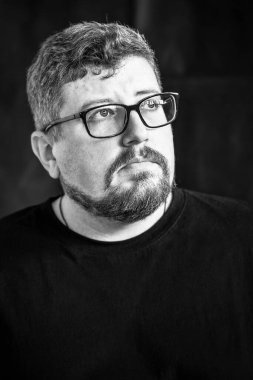 Siyah arka planda gözlüklü, kızıl saçlı, sakallı ve bıyıklı beyaz bir gencin stüdyo resmi..