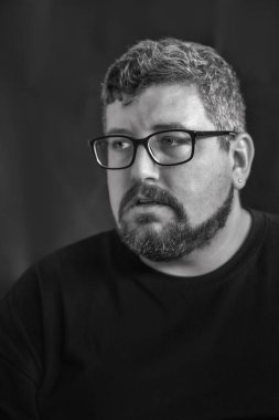 Siyah arka planda gözlük, küpe, kızıl saç, sakal ve bıyık takan beyaz bir adamın stüdyo portresi..