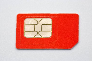 Beyaz bir yüzey üzerinde metalik altın rengi temas noktaları olan parlak turuncu renkli mobil SIM kartın yakın görüntüsü. Bağlantı için modern telekomünikasyon teknolojisi kavramı.