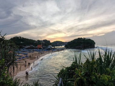 Uçurumun tepesinden gün doğumunda beyaz bir kumsaldaki insanların fotoğrafı.