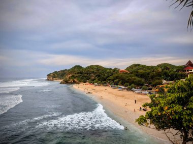 Tepedeki kayalıklarda güzel dalgalarla görülen beyaz bir kumsal fotoğrafı.
