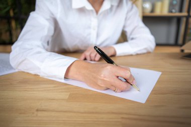 Bir iş kadınının elinde kalem tutarken ve ofiste belge imzalarken.