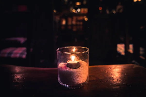 Geïsoleerde theelicht in een glas dat een donkere scène verlicht en reflecties op een houten tafel en een mooie bokeh achtergrond — Stockfoto