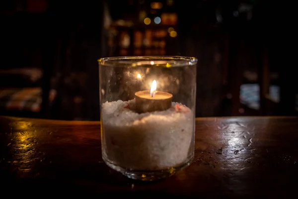 Tealight isolato all'interno di un vetro che illumina una scena buia e riflessioni su un tavolo di legno e un bel sfondo bokeh — Foto Stock