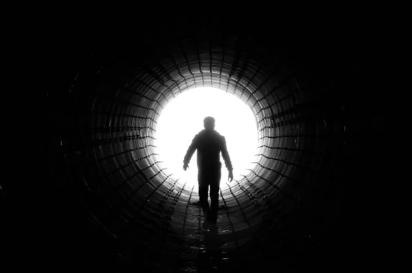 Silhouette of a man walking to the light at the end of a big tunnel. Concept of escape, exit, freedom, clinical death