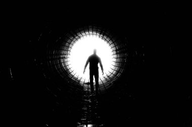 Silhouette of a man walking to the light at the end of a big tunnel. Concept of escape, exit, freedom, clinical death clipart