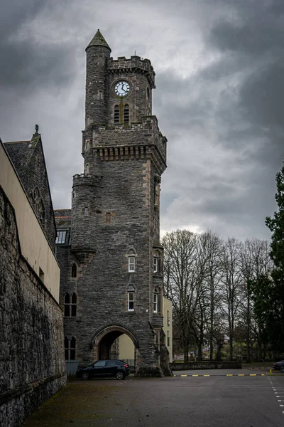 FORT AUGUSTUS, SCOTLAND, DECEMBER 17, 2018: The Abbey Highland Club clock tower, full of mold and lichen in its stone walls, under heavy cloudscape with mountains in the background, aside Loch Ness. — Stock Photo, Image