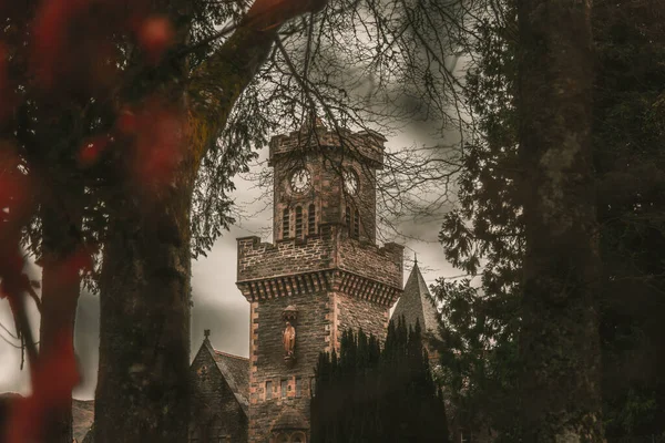 FORT AUGUSTUS, SCOTLAND, DECEMBER 17, 2018: The Abbey Highland Club clock tower, across leaves of trees, under heavy cloudscape with mountains in the background, aside Loch Ness. — Stock Photo, Image