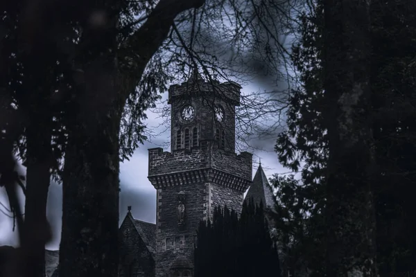 FORT AUGUSTUS, SCOTLAND, DECEMBER 17, 2018: The Abbey Highland Club clock tower, across leaves of trees, under heavy cloudscape with mountains in the background, aside Loch Ness. — Stock Photo, Image