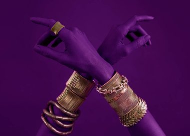 Altın mücevherli leylak kadın elleri. Lilac neon boyalı bir elde Oriental bileklikler. Mor arka planda altın mücevher ve lüks aksesuarlar. Yüksek Moda Sanat Konsepti 