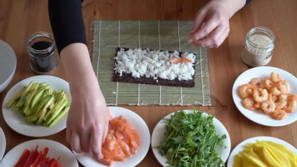 Mujer joven prepara sushi con ingredientes frescos en casa. sobre mesa de madera. — Vídeo de stock