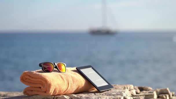 E-reader preto, toalha alaranjada e óculos de sol que colocam em uma rocha perto do mar Istrian — Vídeo de Stock