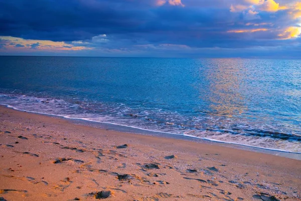 Altın güneşin batışında kışın deniz kenarında. Dramatik kurşun bulutlar. Kumsalda ayak izleri.