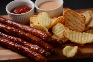 Ev yapımı patates cipsi, sos ve ketçaplı ızgara sosis.