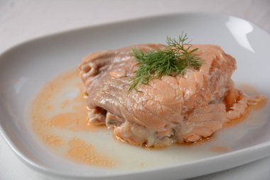 Beyaz tabakta salata yapraklı konserve somon parçaları.