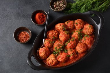 Boulettes de Poisson, Domates soslu kızarmış balık köfteleri beton bir masada siyah bir tabakta malzemelerle.