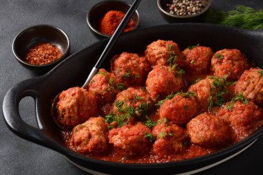 Boulettes de Poisson, Domates soslu kızarmış balık köfteleri beton bir masada siyah bir tabakta malzemelerle.
