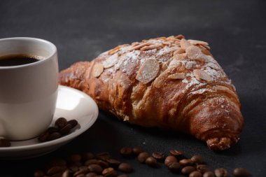 Bir fincan kahveyle taze kruvasan, klasik arka planda kavrulmuş fasulye.