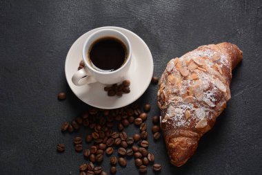 Bir fincan kahveyle taze kruvasan, klasik arka planda kavrulmuş fasulye.