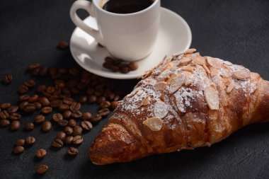 Bir fincan kahveyle taze kruvasan, klasik arka planda kavrulmuş fasulye.