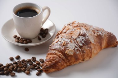 Bir fincan kahveyle taze kruvasan, klasik arka planda kavrulmuş fasulye.