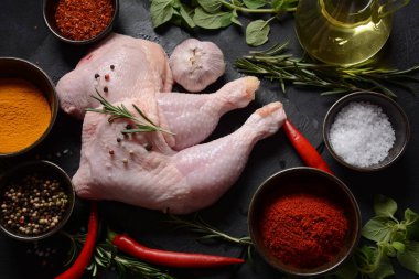 Çiğ tavuk çeyreklikleri, otlu bacaklar ve baharatlar koyu bir arka planda ızgaraya hazır..