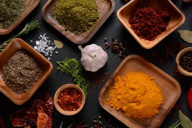 Mutfak masasında çeşitli baharat ve bitkiler var. Koyu arkaplanda yemek pişirmek için çeşitli otlar ve baharatlar.