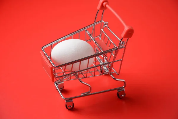 Close up of supermarket grocery push cart for shopping with egg on red background. Concept of shopping. Copy space for advertisement