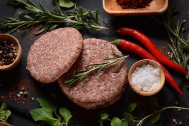 Çiğ etli hamburger köfteleri, baharatlı ve otlu. Beton zeminde hamburgerler.