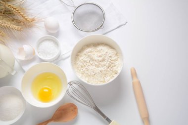 Beyaz arka planda yemek pişirmek için gerekli malzemelerin çerçevesi. Un, yumurta, şeker ve süt beyaz ve ahşap kaselerde. Pişirme ve pişirme konsepti.
